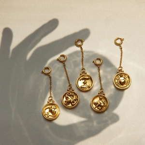 Golden stainless steel zodiac charms with lobster clasps and chains on artistic background