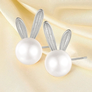 Close-up of cute silver bunny ear stud earrings featuring elegant white pearls on silk