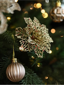 Gros plan sur une fleur dorée pailletée et des boules de Noël de couleur champagne