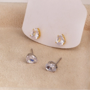 Macro shot of gold and silver pear-cut zircon earrings on a beige velvet background