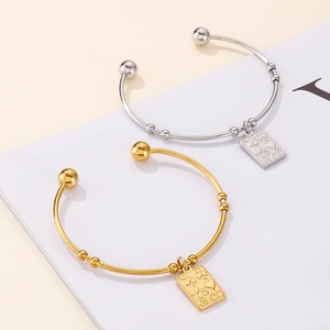 Detail of gold and silver stainless steel bangles with rectangular engraved pendants