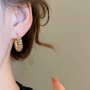 Nahaufnahme eleganter goldener Creolen mit funkelnden Strasssteinen an einem Model