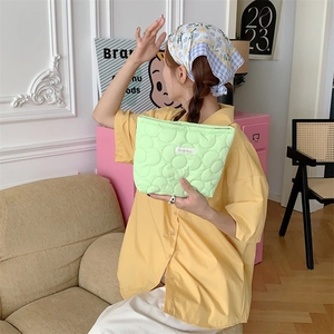 Close-up of a light green quilted makeup bag held by a model in a modern interior
