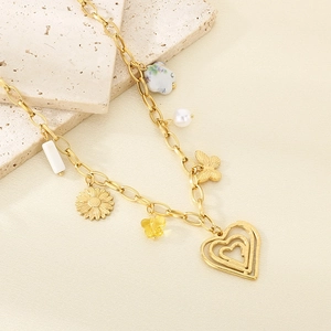Detail of gold necklace with heart, butterfly, sunflower and ceramic pendants on beige stone