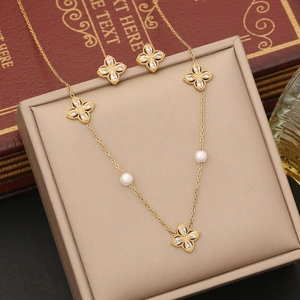 Golden flower necklace and earrings set with clover charms, zircons, and pearls in a box