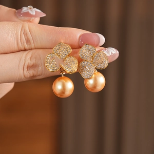 Macro detail of gold plated clover earrings with pave zircon and elegant golden pearl
