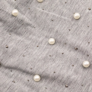 Détail du tissu tricoté gris avec perles blanches parsemées et clous décoratifs en métal