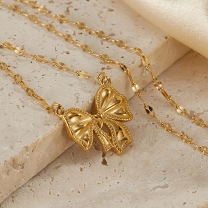 Detailed macro view of a gold bow pendant necklace on elegant silk and marble