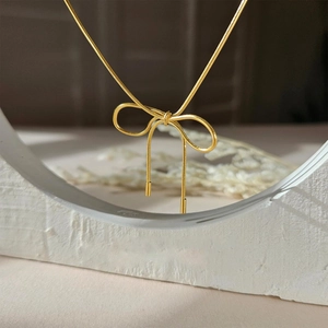 Elegant gold bow pendant necklace with thin snake chain on a minimalist stone display