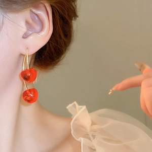 Close-up of model wearing bright red cherry stud earrings with gold metal stems