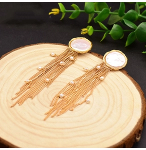 Detail of gold tassel earrings with white mother of pearl and small pearls on wood