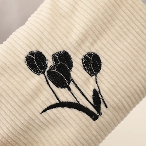 Detail of cream corduroy fabric with black tulip embroidery and ribbed texture