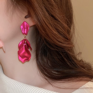 Close-up of matte magenta petal-shaped drop earrings worn by a model in a side view