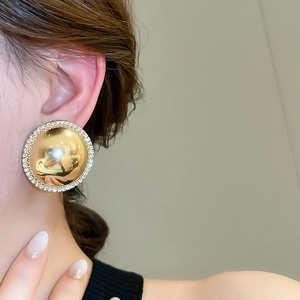 Close-up of golden dome stud earrings with sparkling rhinestone trim on female model