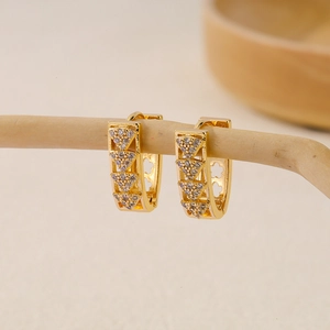 Close-up of gold V-shaped zircon earrings hanging on a natural branch with bokeh effect