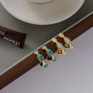 Detail view of C-shaped stainless steel earrings with white pearls and blue turquoise stones