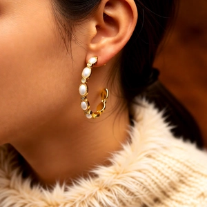 Detailed view of C-shaped 18K gold earrings with white pearls and small rhinestones
