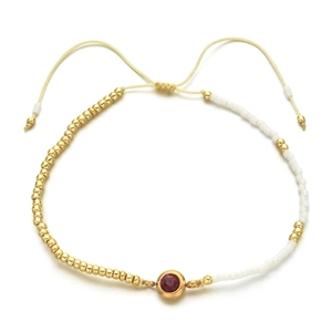 Detail of adjustable handmade beaded bracelet with golden beads and red zircon stone
