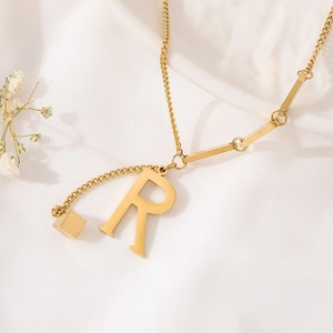 Macro detail of gold-plated titanium necklace with letter R pendant and square charm