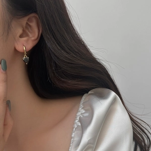Close-up of a gold hoop earring with a black heart pendant worn by a model