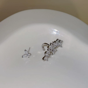 Macro shot of silver butterfly stud and zircon ear cuff set on a white ceramic tray