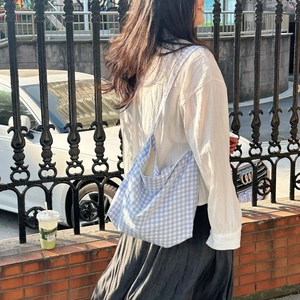 Detailed outdoor shot of a blue and white checkered canvas tote bag on the shoulder