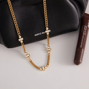 Détail d'un collier en chaîne dorée avec strass sur un sac en cuir noir élégant