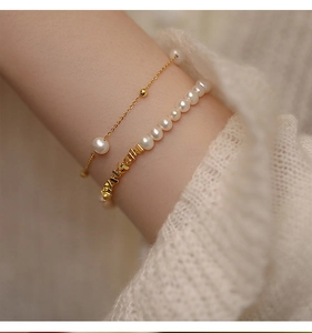 Close-up of layered pearl bracelet with gold letter charms on a soft knit sleeve