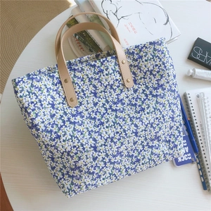 Macro detail of purple floral tote bag with brown leather handle and gold rivet hardware