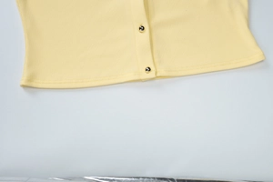 Détail de la maille côtelée et des boutons dorés sur le cardigan ajusté jaune clair
