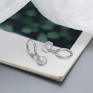 Detailed view of S925 silver shell earrings with pearl inlay resting on a magazine