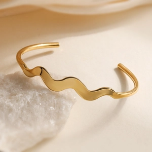 Minimalist 18K gold plated stainless steel wave bangle on a white natural stone base