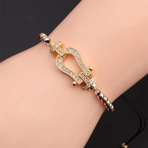 Detail of a horseshoe-shaped gold clasp set with white zircon on a black cord bracelet