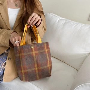 Detail of checkered woolen fabric lunch bag with yellow canvas handle and bronze button