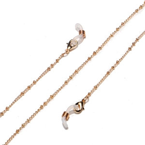 Macro detail of golden metal eyeglass chain with white silicone loops and lobster clasp