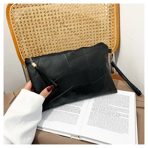 Detail of a black textured envelope clutch with gold metal hardware and tassel charm