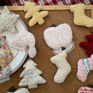 Flat lay of handmade knitted Christmas ornaments with star and tree shapes on cork