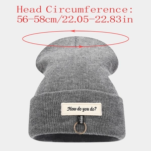 Détail du bonnet en maille gris foncé avec écusson lettré et anneau métal