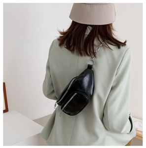 Close-up of black leather chest bag with silver chain strap worn over a light green blazer