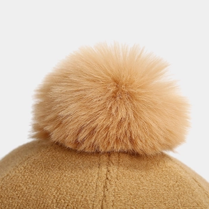 Close-up of fluffy faux fur pom-pom and soft brown knit texture on a winter baseball cap
