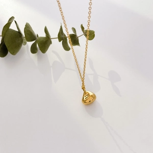 Detailed close-up of a polished gold teardrop pendant on a fine cross chain over white background