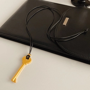 Détail d'un pendentif clé doré avec cordon noir sur une surface en cuir texturé