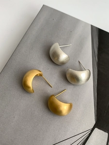 Detailed view of minimalist brushed gold and silver geometric stud earrings on magazine