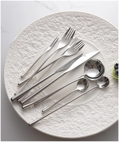 Macro view of mirror finish stainless steel cutlery set on a white textured plate