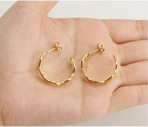 Detailed close-up of gold textured C-shape hoop earrings held in hand for size scale