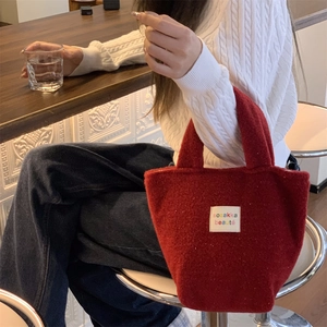 Detail of dark red felt tote bag with white fabric label held by person in a white sweater