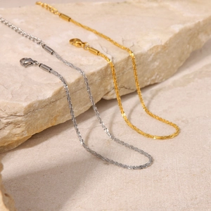 Macro detail of elegant wavy snake chain anklets in gold and silver finish on a stone