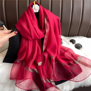Detail of red silk wool scarf featuring elegant gold stripes and shimmering texture