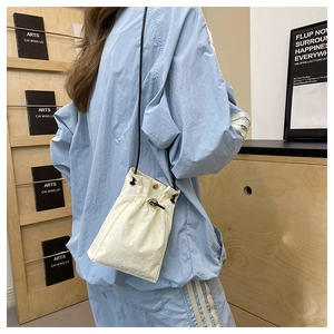 Minimalist beige drawstring crossbody bag with black thin strap worn by a model