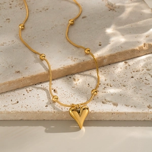 Close-up of golden heart pendant necklace with beaded snake chain on a stone background